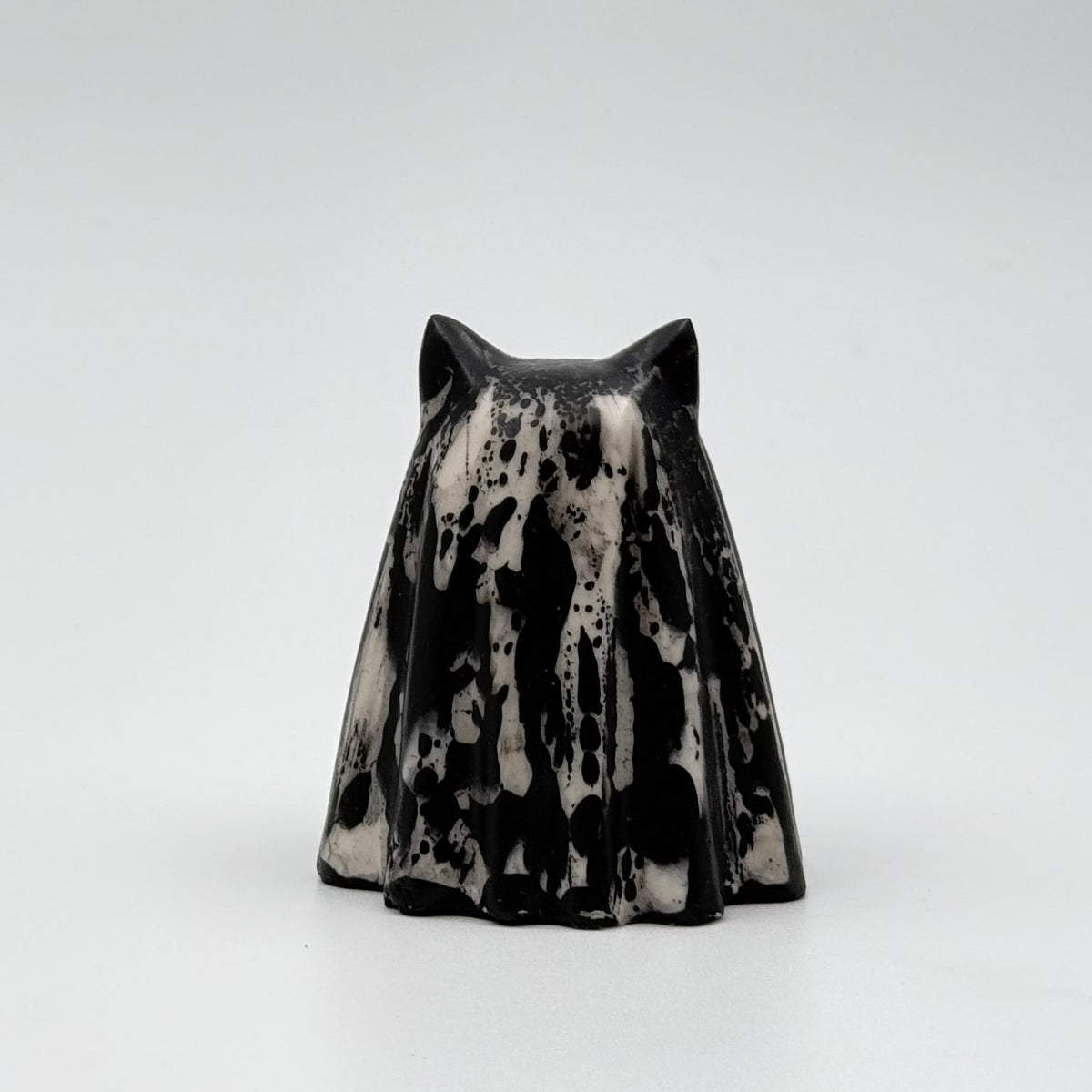 A handmade ghost cat figurine by The Nordic Ghost Merchants. The ghost ornament is bone white with black, bark like patterning. Rear view on a grey studio background.