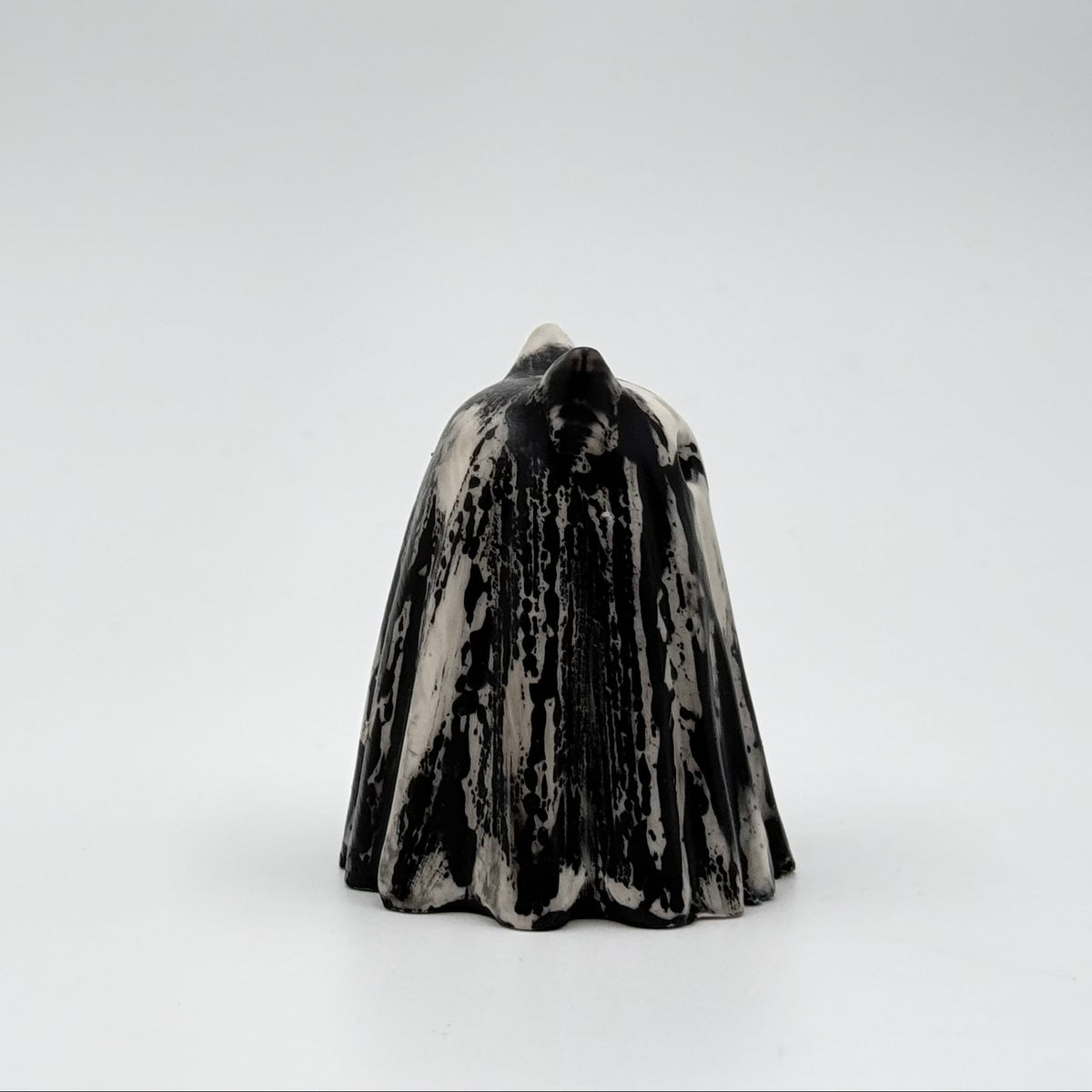 A handmade ghost cat figurine by The Nordic Ghost Merchants. The ghost ornament is bone white with a black, bark like pattern. Side view on a grey studio background.