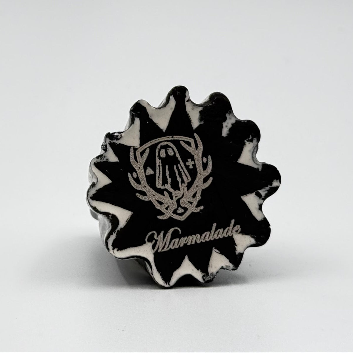 A handmade ghost cat figurine made by The Nordic Ghost Merchants. The image shows the base of the ghost ornament, painted black with the brand logo - a coat of arms with a sheet ghost in the centre.