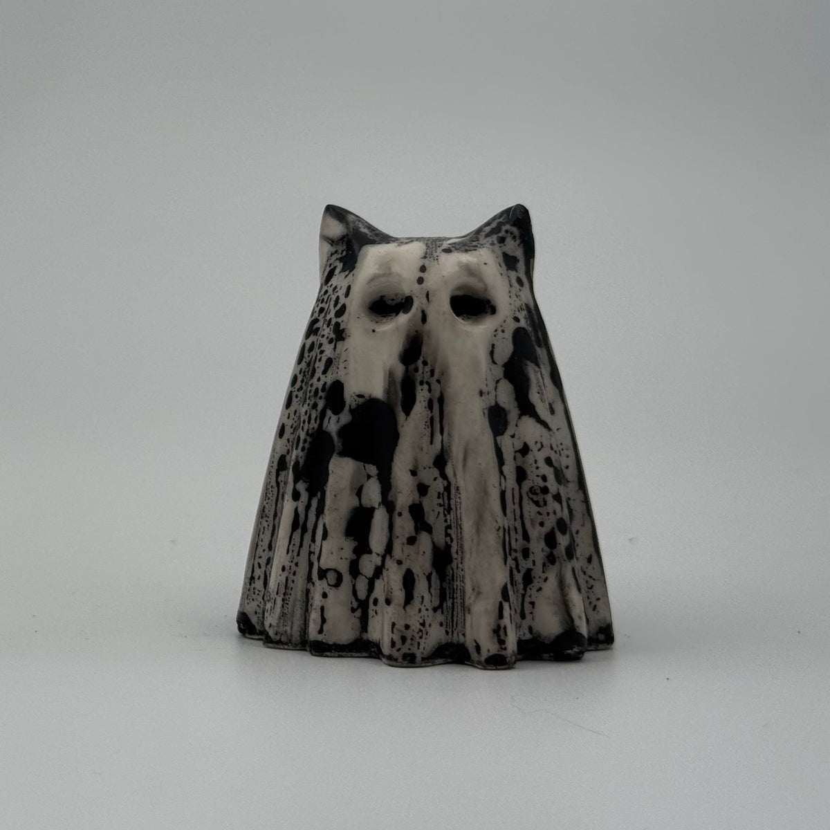 An ivory ghost cat figurine with dramatic black, bark like patterning, made by The Nordic Ghost Merchants. Front view.