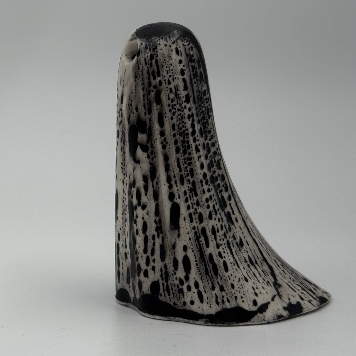 An ivory ghost figurine with dramatic black, bark like patterning, made by The Nordic Ghost Merchants. Side view.