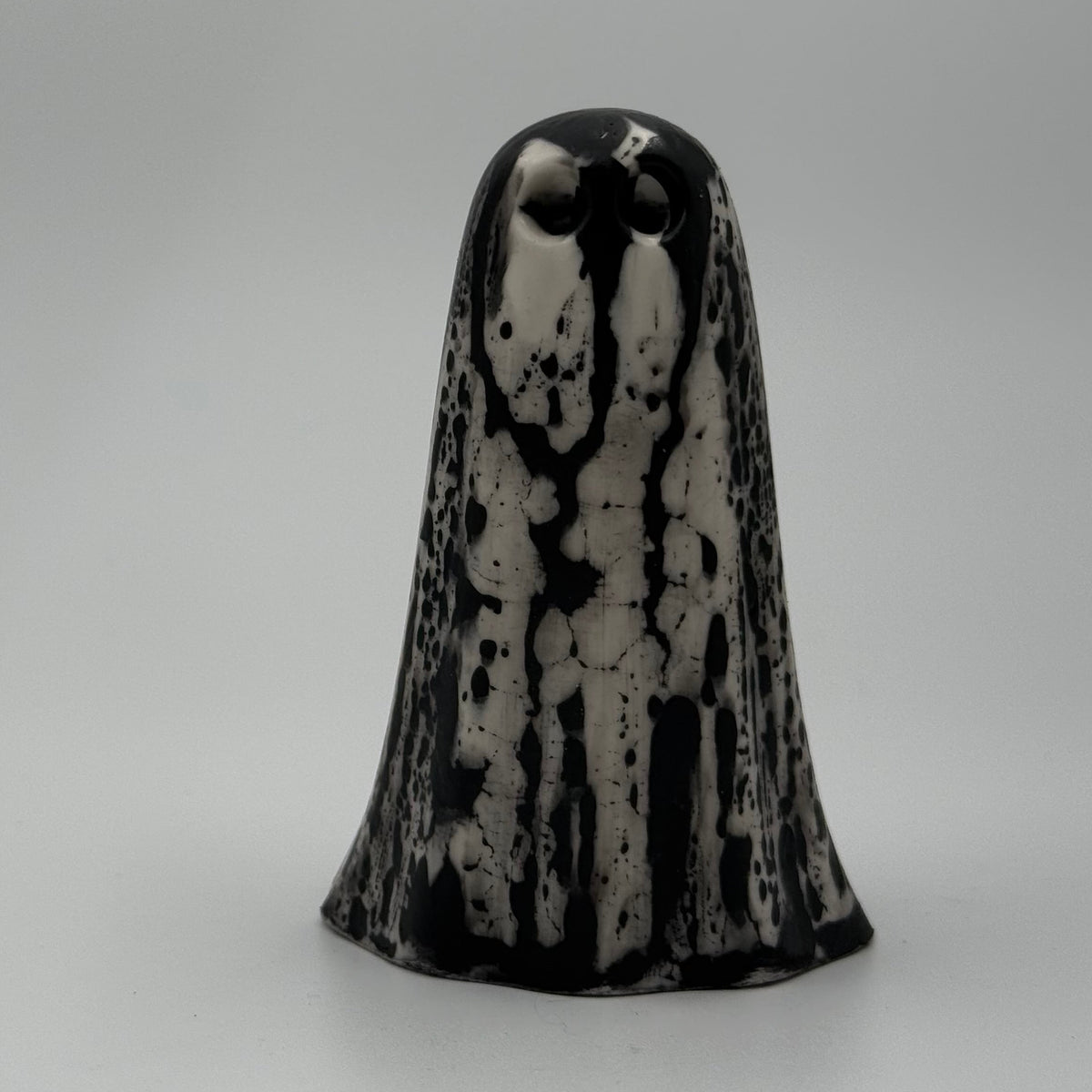 An ivory coloured ghost ornament with dramatic black, bark like patterning, made by The Nordic Ghost Merchants. Front view.