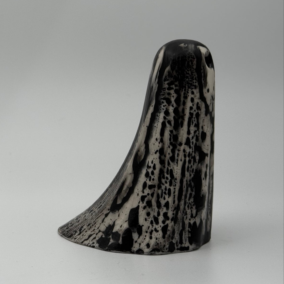 An ivory coloured ghost ornament with dramatic black, bark like patterning, made by The Nordic Ghost Merchants. Front view.