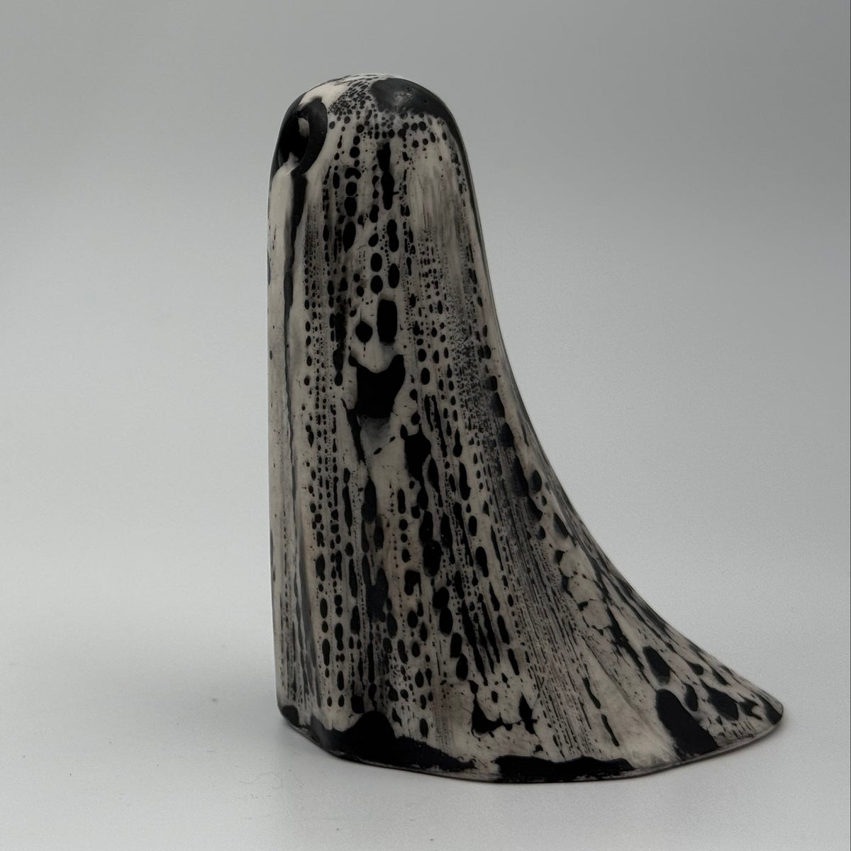 An ivory coloured ghost ornament with dramatic, black bark like patterning, made by The Nordic Ghost Merchants. Side view.