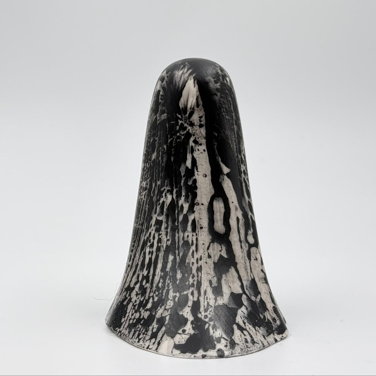 A handmade ghost figurine made by The Nordic Ghost Merchants. The base of the ghost is bone white and it has black, bark like patterning over the full body of the ghost ornament. Rear view against a grey studio background.