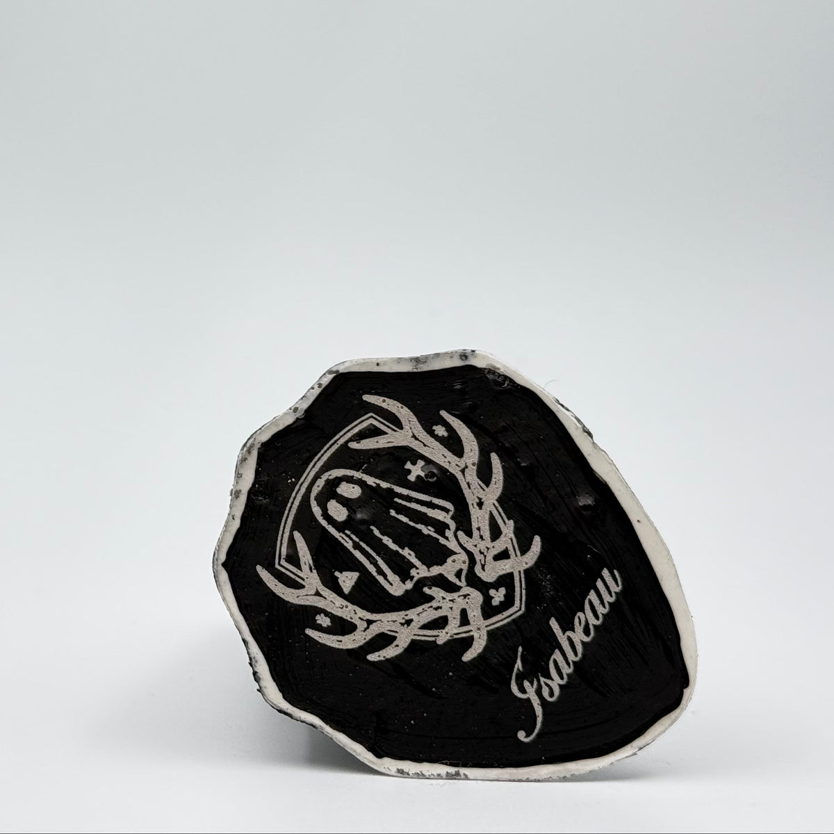 A Handmade Ghost Figurine made by The Nordic Ghost Merchants. The view is of the base of the ghost, engraved with the brand logo - a coat of arms with a sheet ghost in the middle.