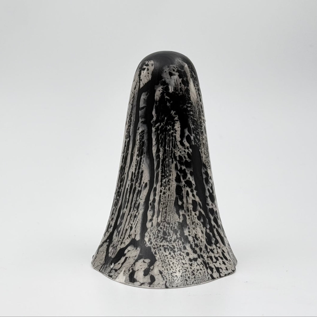 A handmade ghost figurine made by The Nordic Ghost Merchants in Denmark. The ghost is bone white with black, bark like patterning. Rear view on a grey studio background.