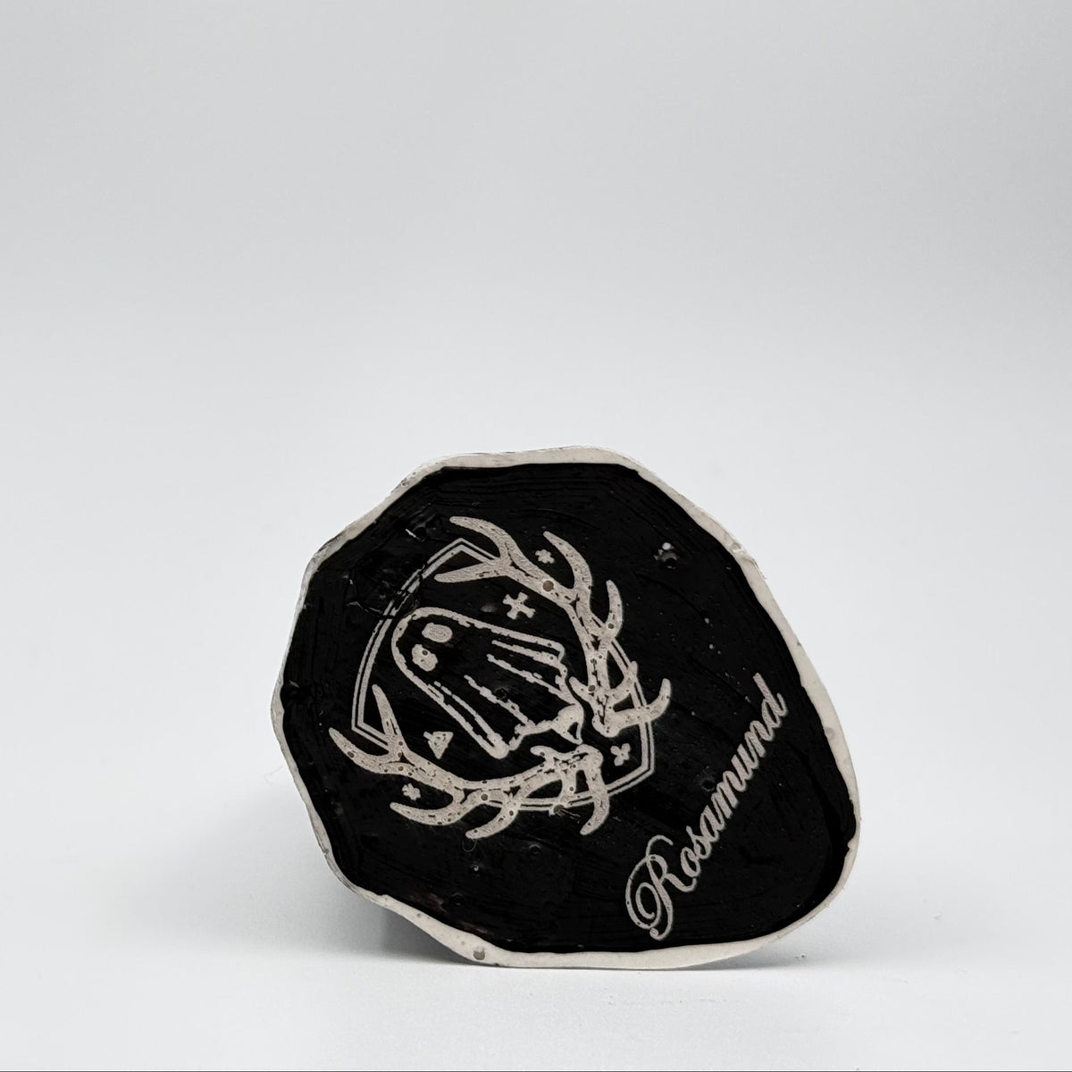 A handmade ghost figurine made by The Nordic Ghost Merchants. The view is of the base of the ghost ornament, painted black and engraved with the brand logo - a coat of arms with a sheet ghost in the centre.