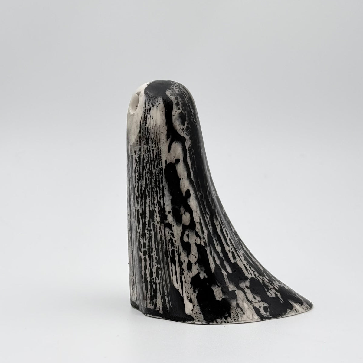 A handmade ghost figurine made by The Nordic Ghost Merchants. The ghost is bone white with black, bark like patterning. Side view on a grey studio background.