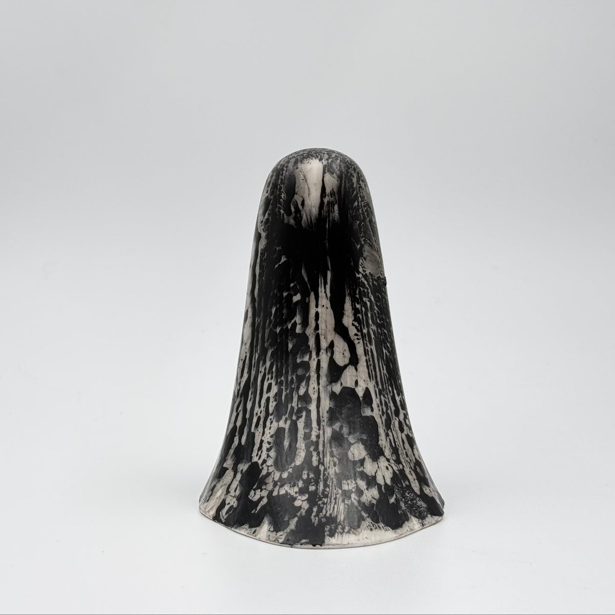 A handmade ghost figurine made by The Nordic Ghost Merchants. The ghost is bone white with black, bark like patterning. Rear view on a grey studio background.