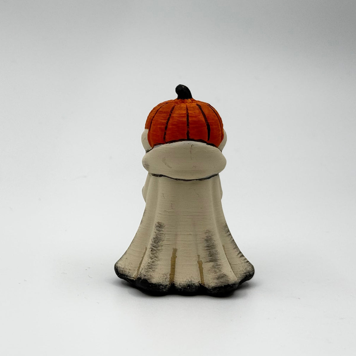 A hand painted folklore figurine made by The Nordic Ghost Merchants in Denmark. The figurine has a carved pumpkin head and is robed in cream cloth while he clutches an autumn leaf. Rear view on a grey studio background.