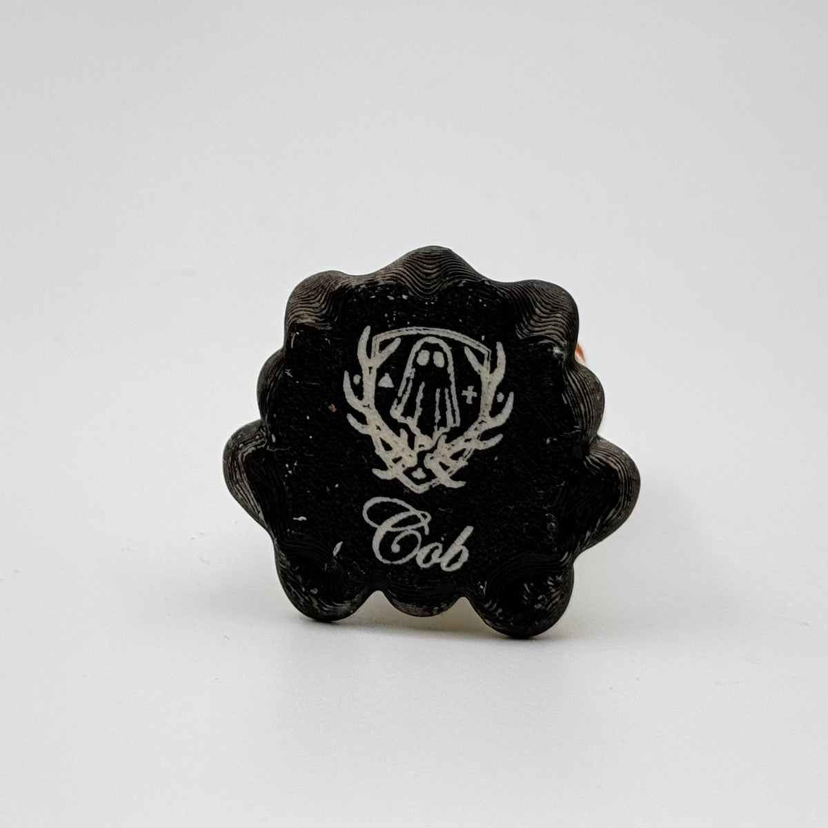 A hand painted folklore figurine made by The Nordic Ghost Merchants in Denmark. The image shows the base of the folklore ornament, painted black and engraved with the brand logo - a coat of arms with a sheet ghost in the centre.