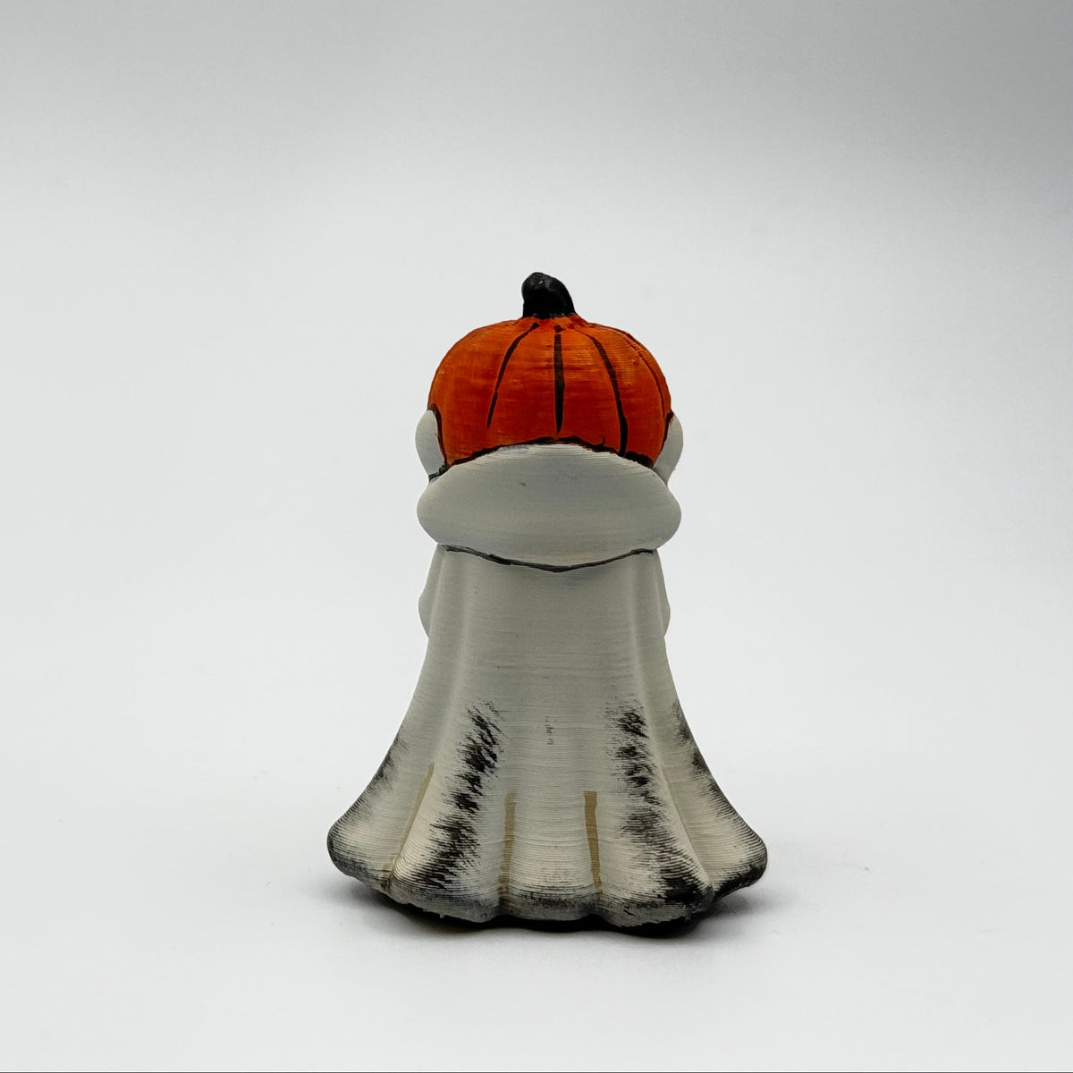 A hand painted folklore figurine made by The Nordic Ghost Merchants in Denmark. The figurine has a carved pumpkin head and is robed in cream cloth while he clutches an autumn leaf. Rear view on a grey studio background.