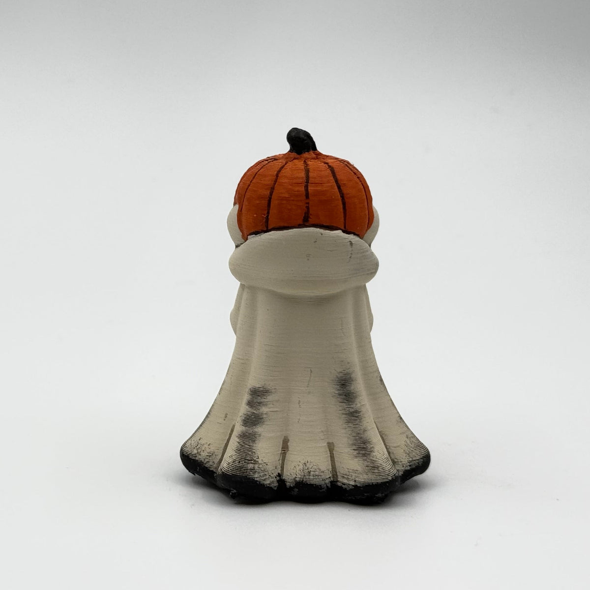 A hand painted folklore figurine made by The Nordic Ghost Merchants in Denmark. The figurine has a carved pumpkin head and is robed in cream cloth while he clutches an autumn leaf. Rear view on a grey studio background.
