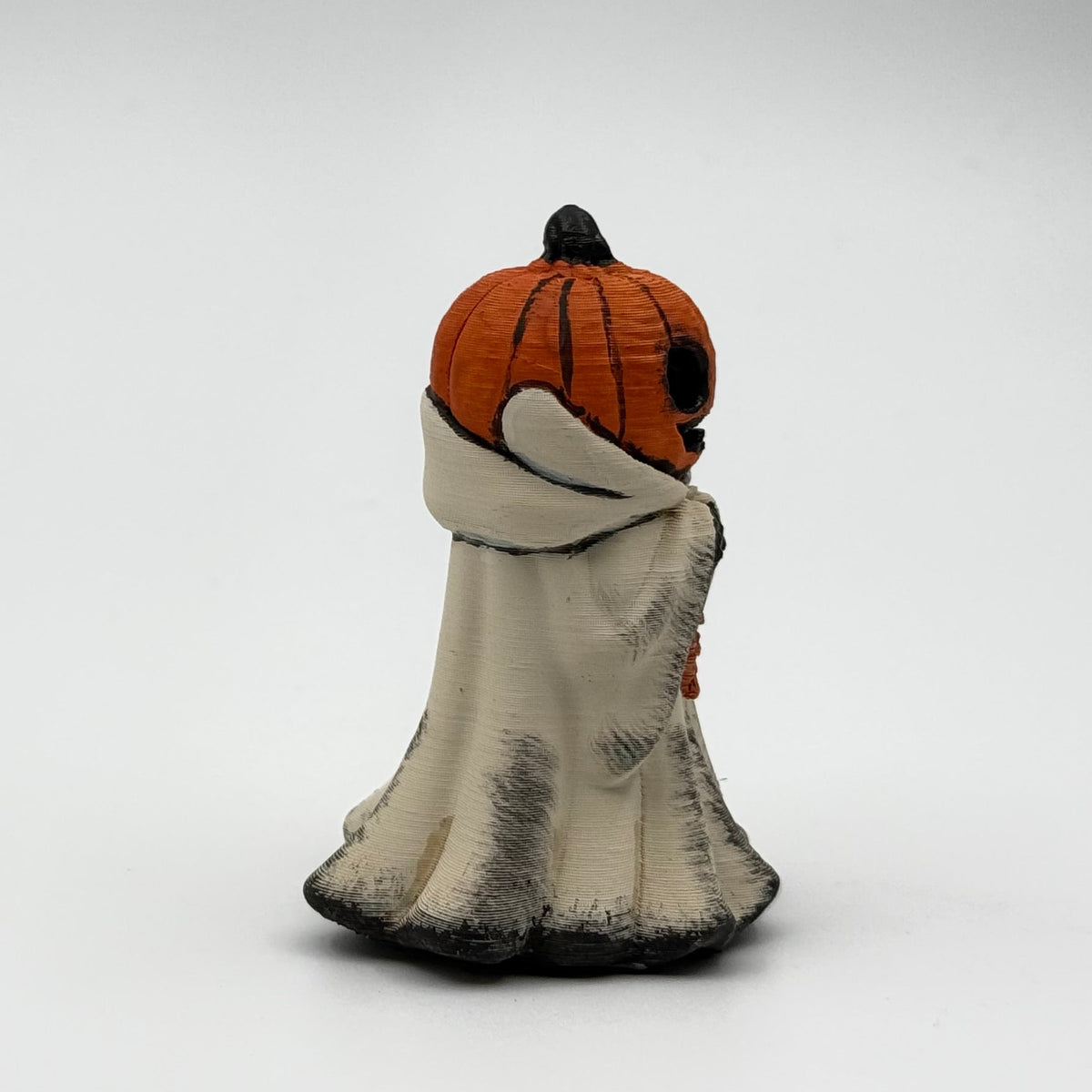 A hand painted folklore figurine made by The Nordic Ghost Merchants in Denmark. The figurine has a carved pumpkin head and is robed in cream cloth while he clutches an autumn leaf. Front view on a grey studio background.