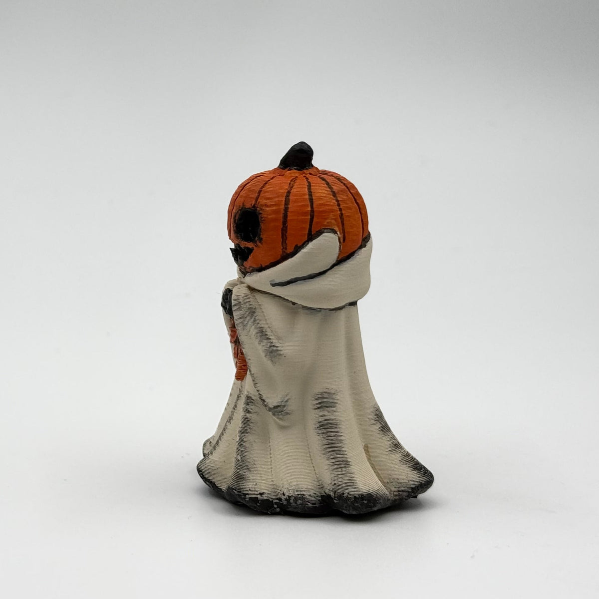 A hand painted folklore figurine made by The Nordic Ghost Merchants in Denmark. The figurine has a carved pumpkin head and is robed in cream cloth while he clutches an autumn leaf. Front view on a grey studio background.