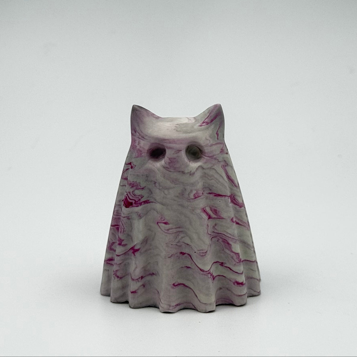 A small grey and white marbled ghost cat figurine by The Nordic Ghost Merchants. The ghost cat has raspberry pink ripples throughout. Front view on a grey studio background.