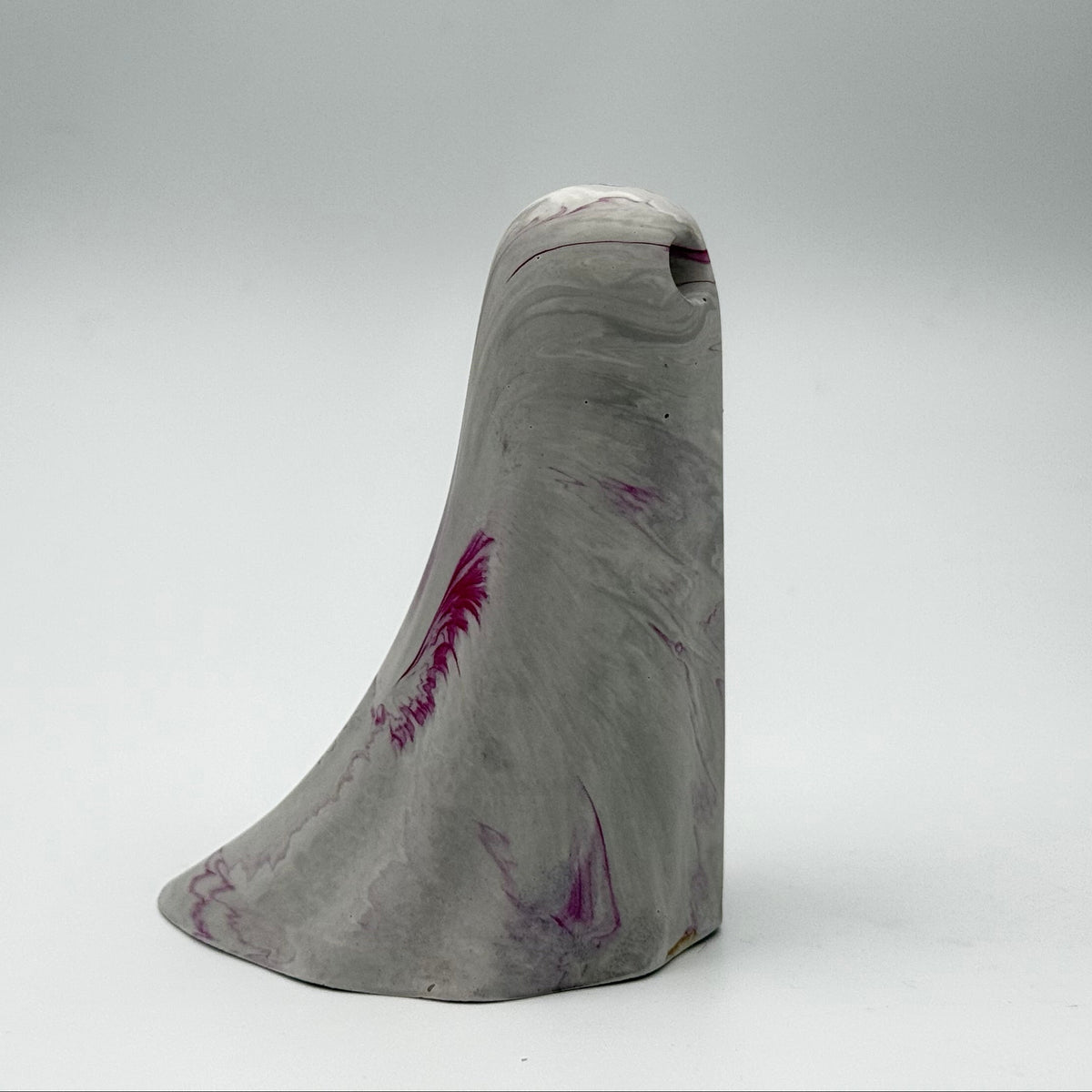 A grey and white marbled handmade ghost figurine made by The Nordic Ghost Merchants. The ghost has ripples of cerise pink throughout. Side view on a neutral grey studio background.