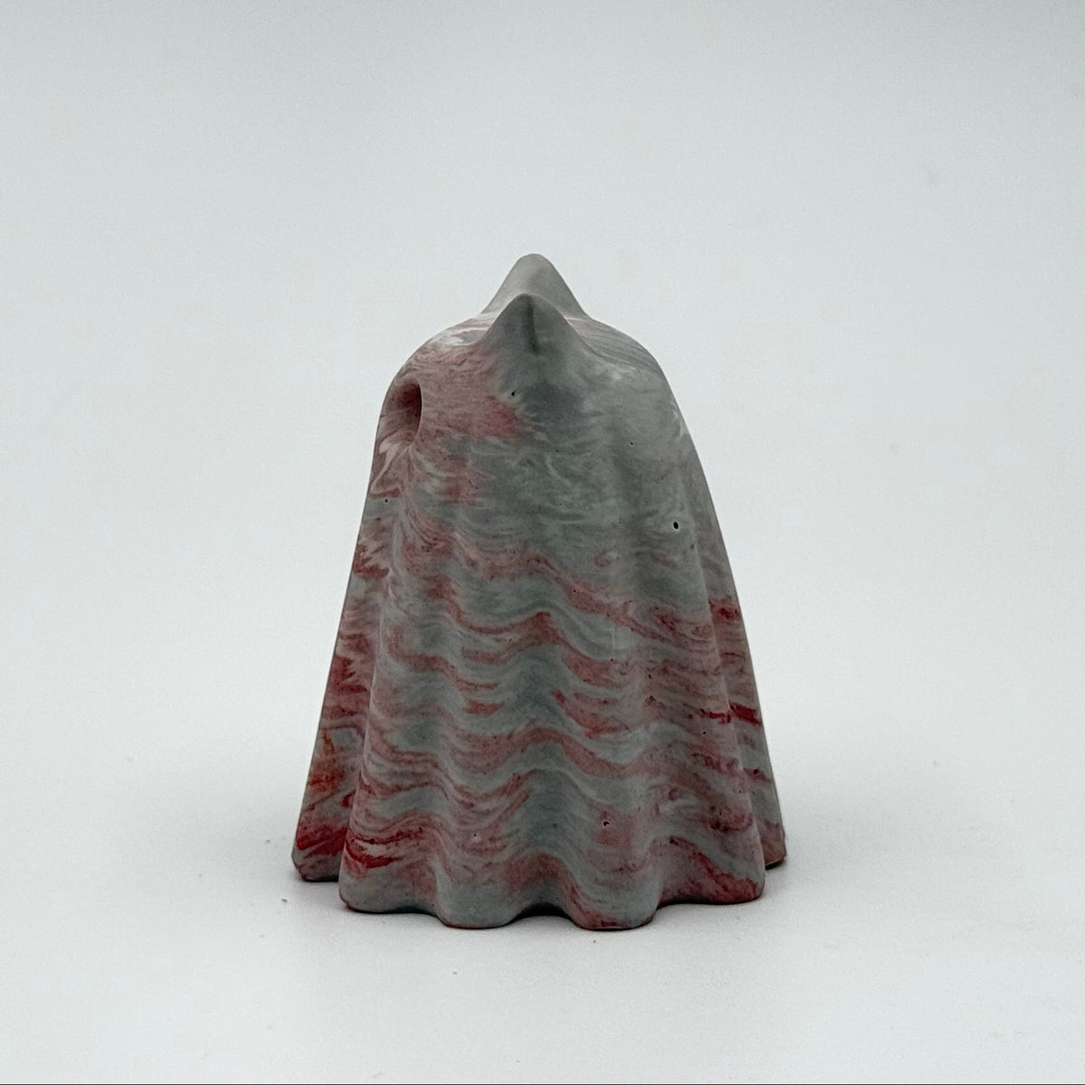 A small grey and white marbled ghost cat figurine. The figurine has dark red ripples running throughout and is handmade by The Nordic Ghost Merchants. On a grey studio background.