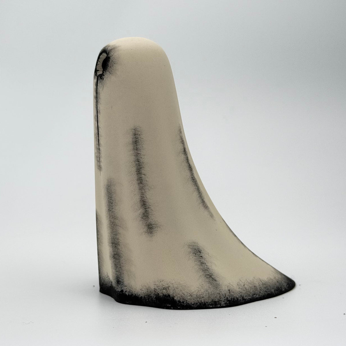 An ivory handmade ghost figurine made by The Nordic Ghost Merchants. The ghost has hand painted black eyes and tear details. Side view on a grey studio background.