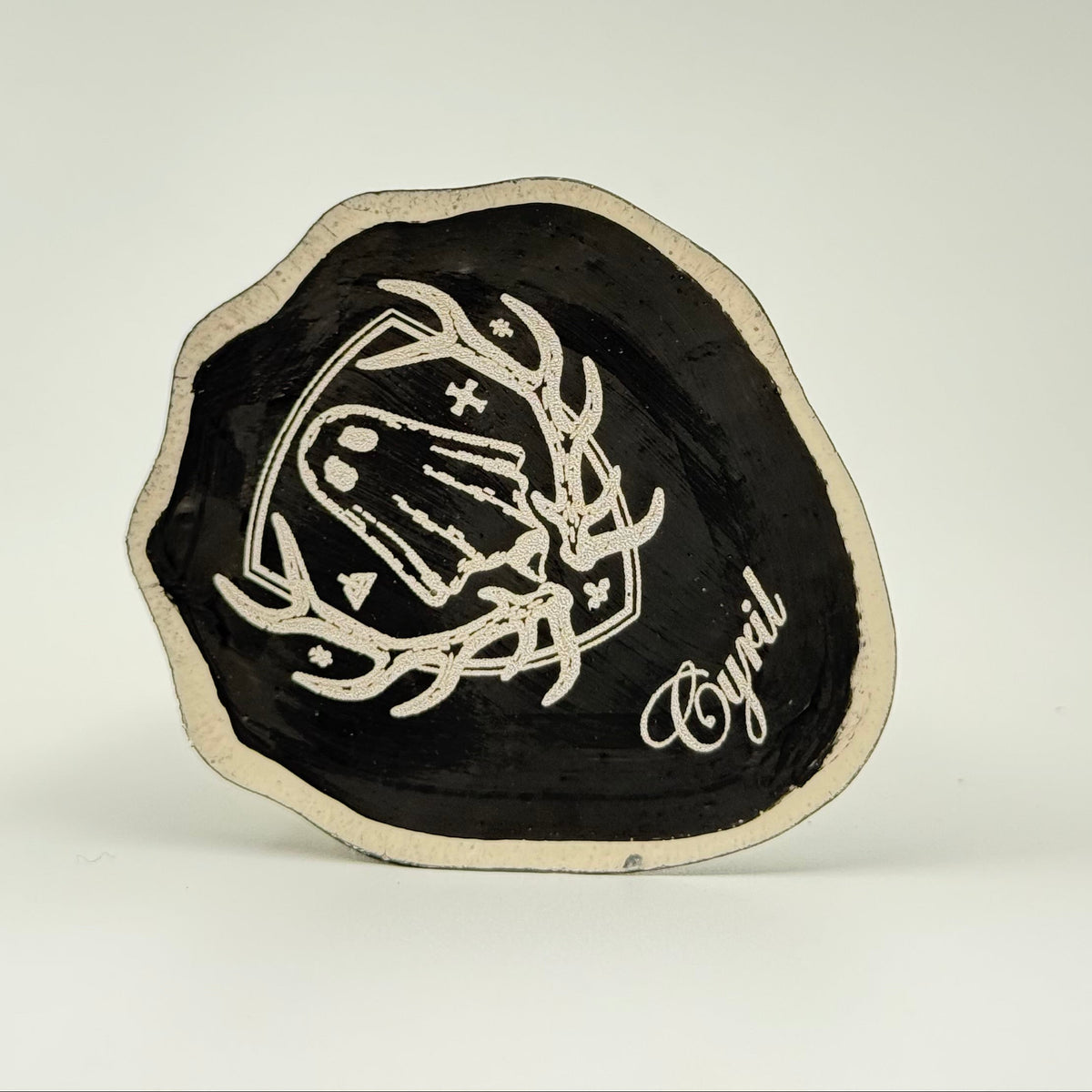 An ivory coloured handmade ghost figurine by The Nordic Ghost Merchants. The image is of the base of the ghost, painted black and engraved with the brand logo - a coat of arms with a sheet ghost inside.