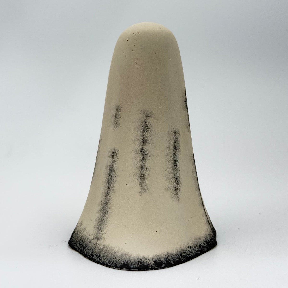 A handmade ghost figurine made by The Nordic Ghost Merchants. The body of the ghost is an ivory cream colour with distressed black details around the base and along the folds of the sheet ghost. Rear view on a grey studio background.