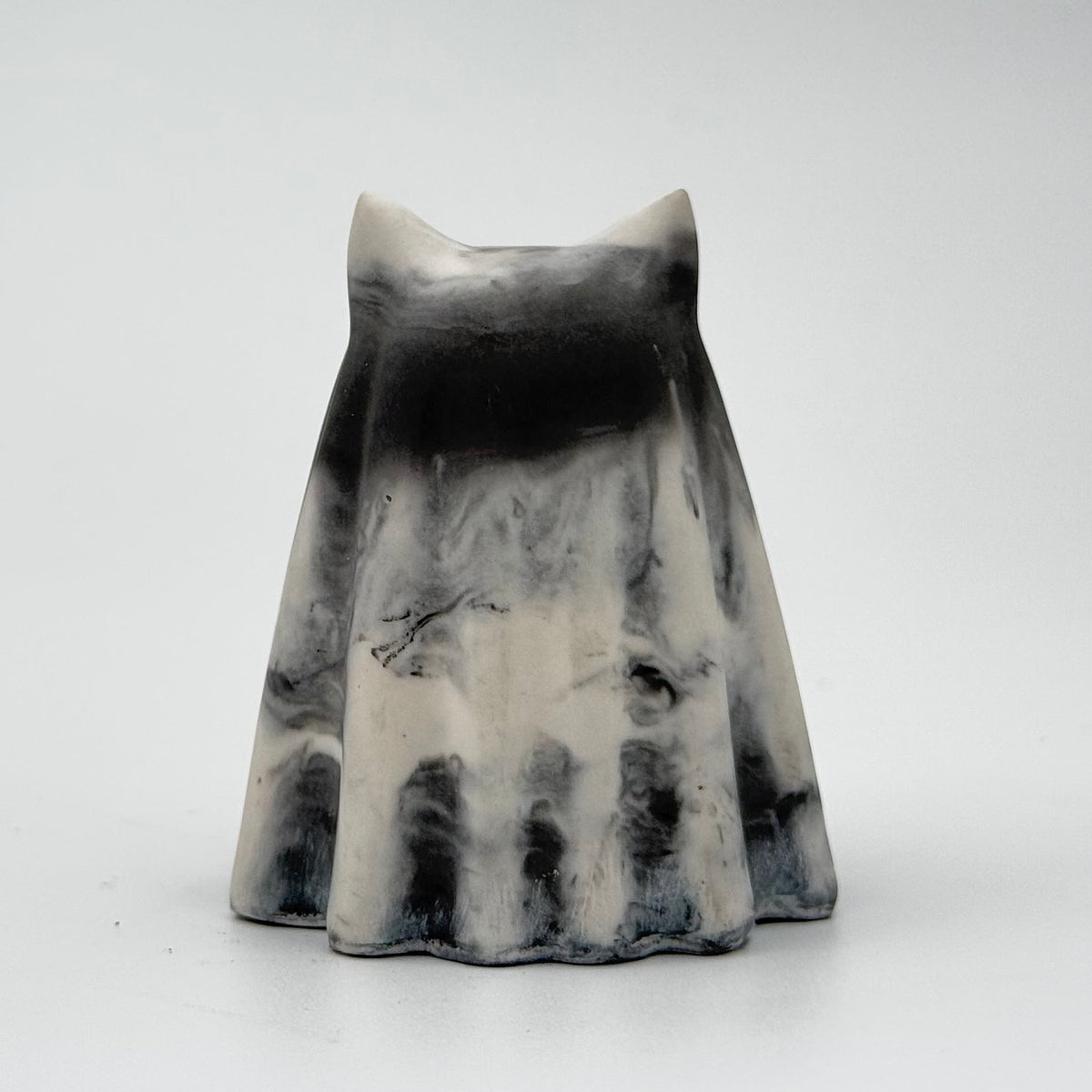 A grey and white marbled handmade ghost cat figurine by The Nordic Ghost Merchants. The colours are in a smoky or fog-like pattern. Rear view on a grey studio background.