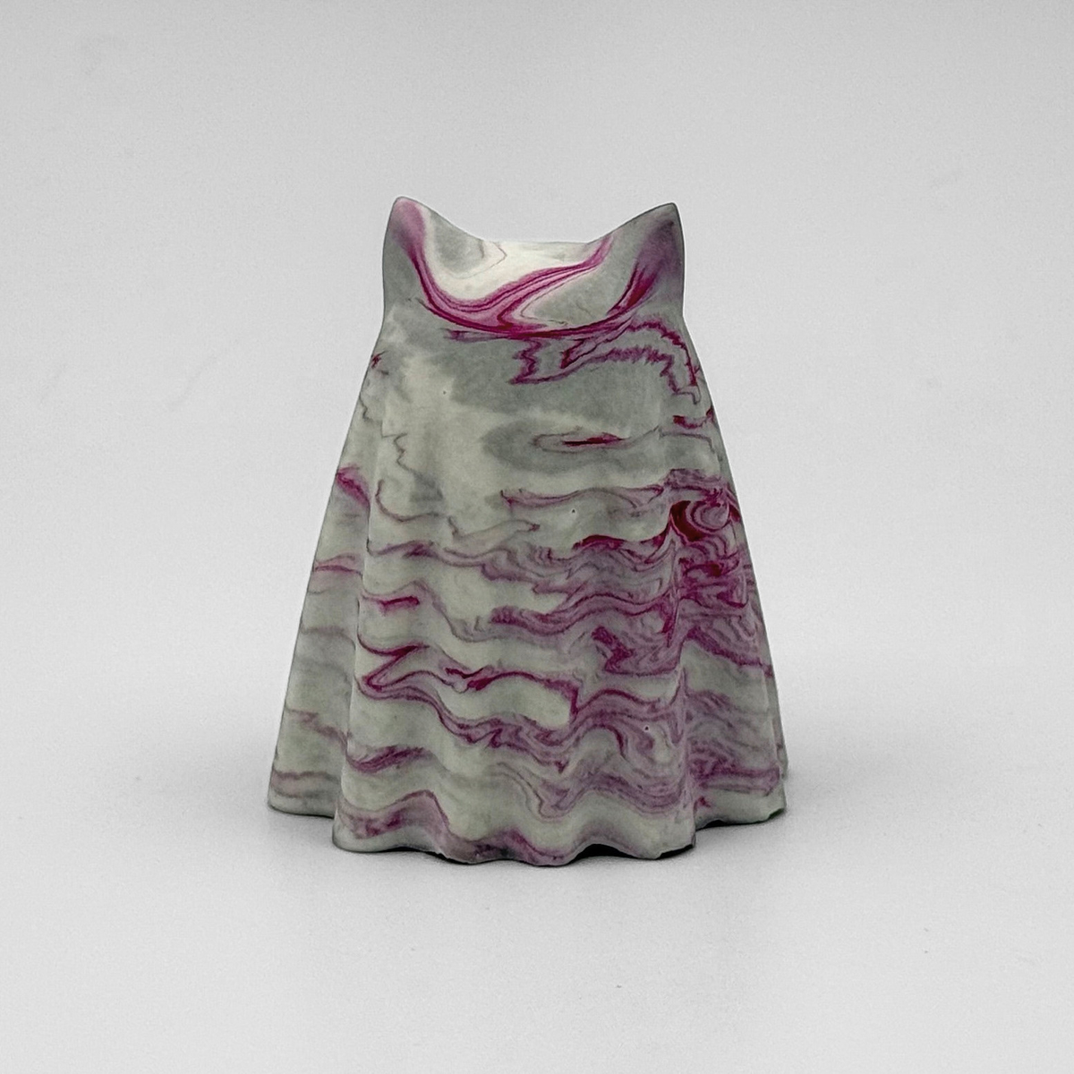 A small grey and white marbled ghost cat figurine by The Nordic Ghost Merchants. The ghost cat has raspberry pink ripples throughout. Rear view on a grey studio background.