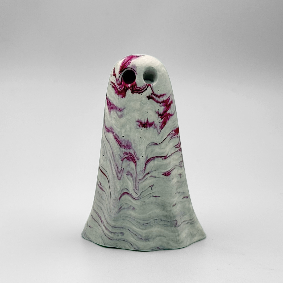 A white and grey marbled handmade ghost figurine by The Nordic Ghost Merchants. The ghost has cerise pink ripples running through it. Front view on a grey studio background.