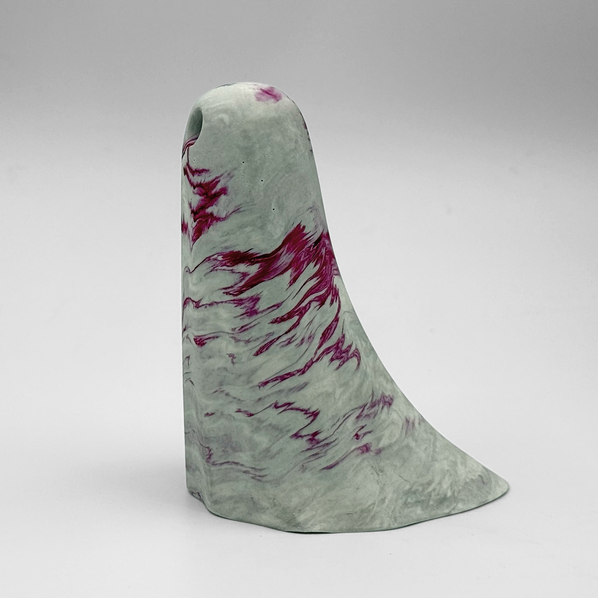 A white and grey marbled handmade ghost figurine by The Nordic Ghost Merchants. The ghost has cerise pink ripples running through it. Side view on a grey studio background.
