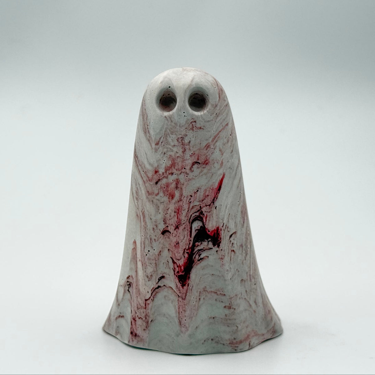 A small grey and white handmade ghost figurine by The Nordic Ghost Merchants. The ghost has dark red ripples throughout. Front view on a grey studio background.