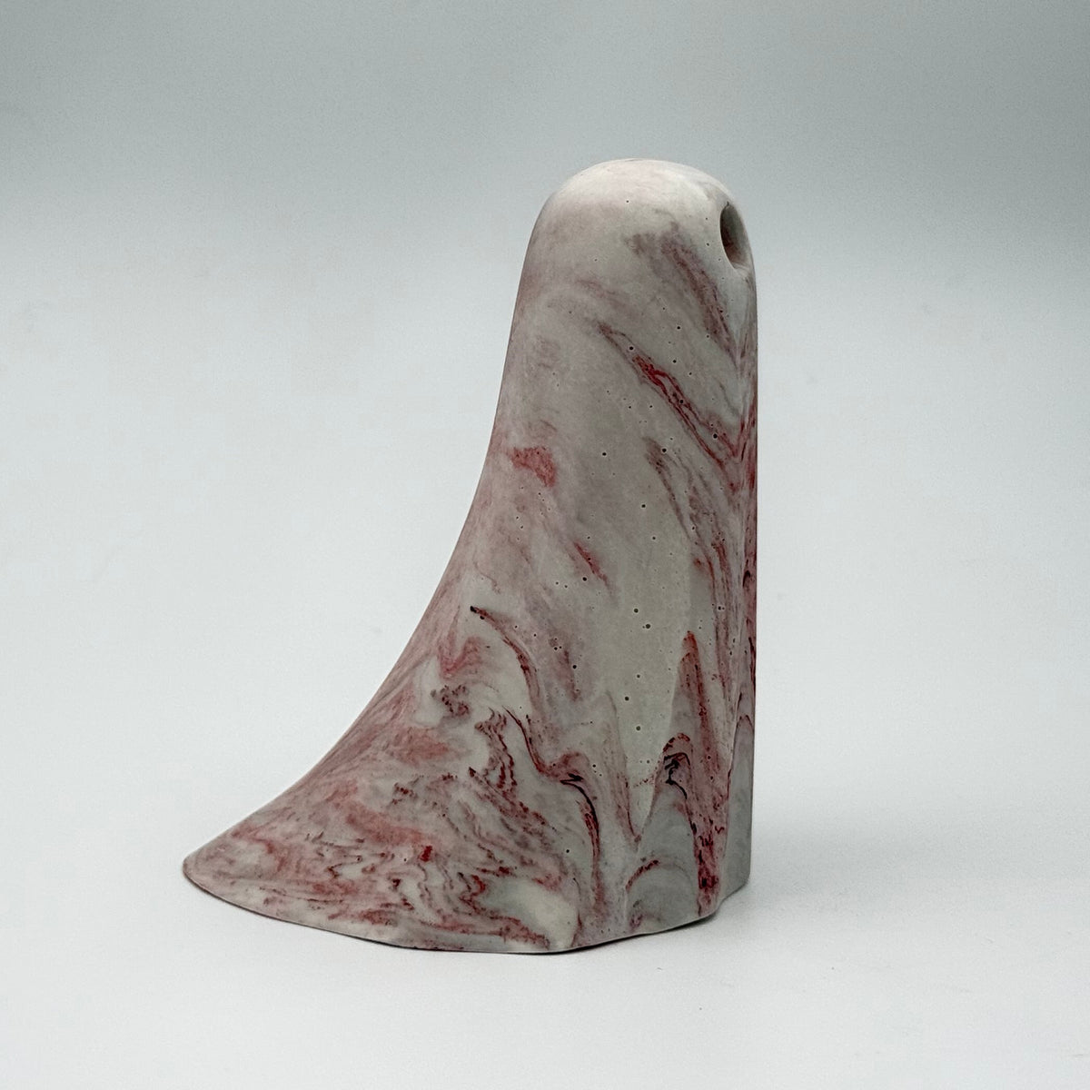 A small grey and white marbled handmade ghost figurine made by The Nordic Ghost Merchants. The ghost has dark red ripples throughout. Side view on a grey studio background.