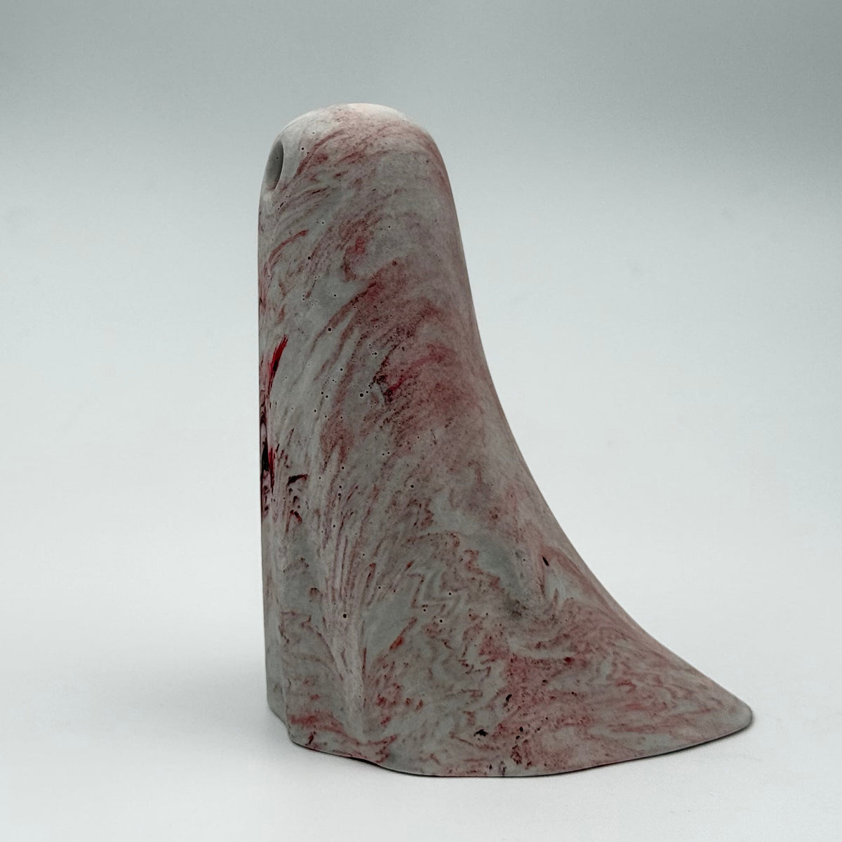 A small grey and white ghost figurine handmade by The Nordic Ghost Merchants. The ghost has dark red ripples throughout. Side view on a grey studio background