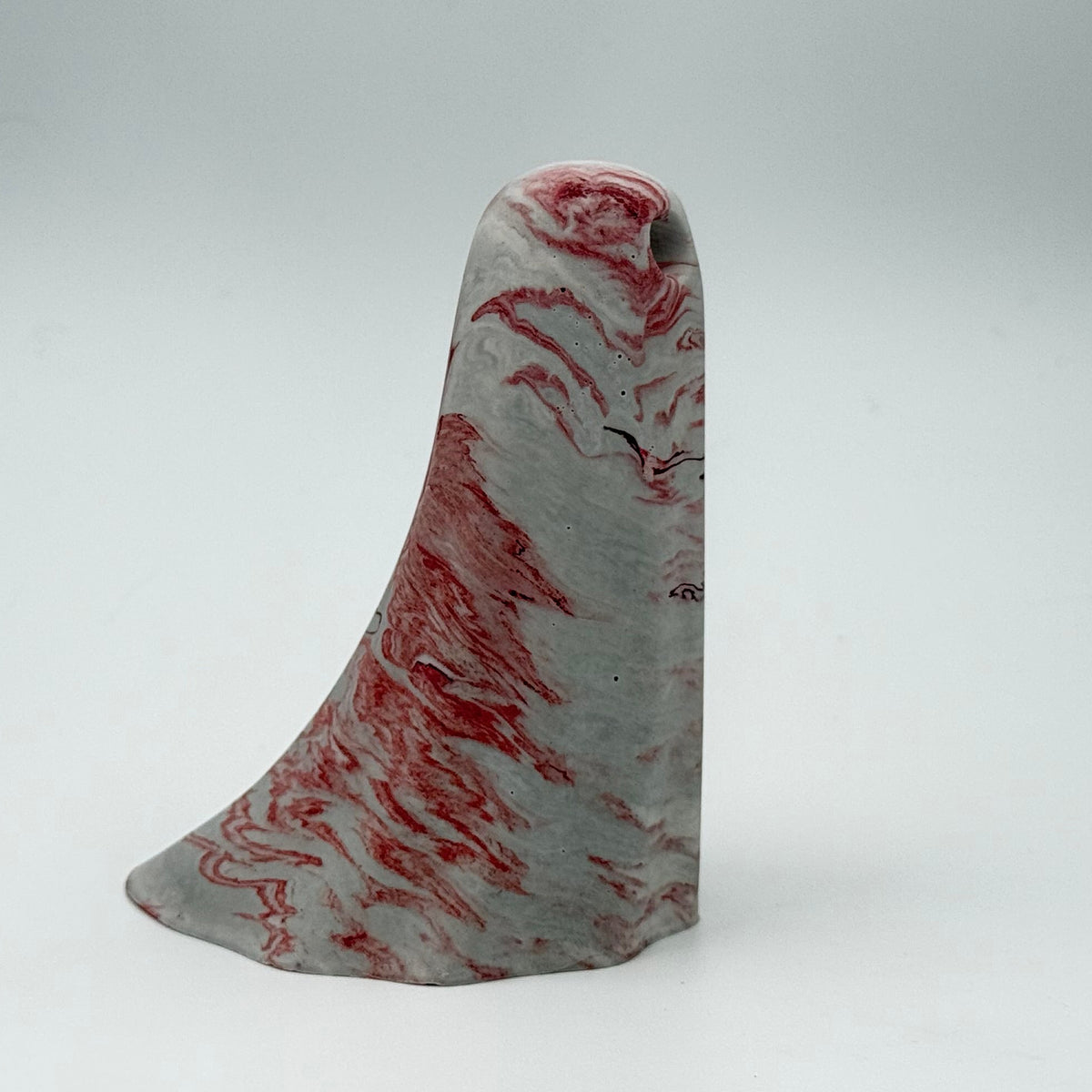 A small grey and white marbled ghost figurine made by The Nordic Ghost Merchants. The ghost has dark red ripples running through it. Side view on a grey studio background.