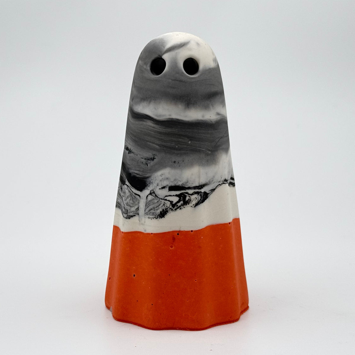A handmade ghost figurine made by The Nordic Ghost Merchants in Denmark. The body of the ghost is grey and white marbled. The bottom quarter is a pumpkin orange. Front view on the grey studio background.