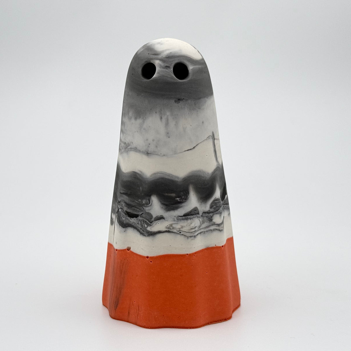 A handmade ghost figurine made by The Nordic Ghost Merchants in Denmark. The body of the ghost is a grey & white marbled colour. The bottom quarter is a pumpkin orange. Front view on a grey studio background.