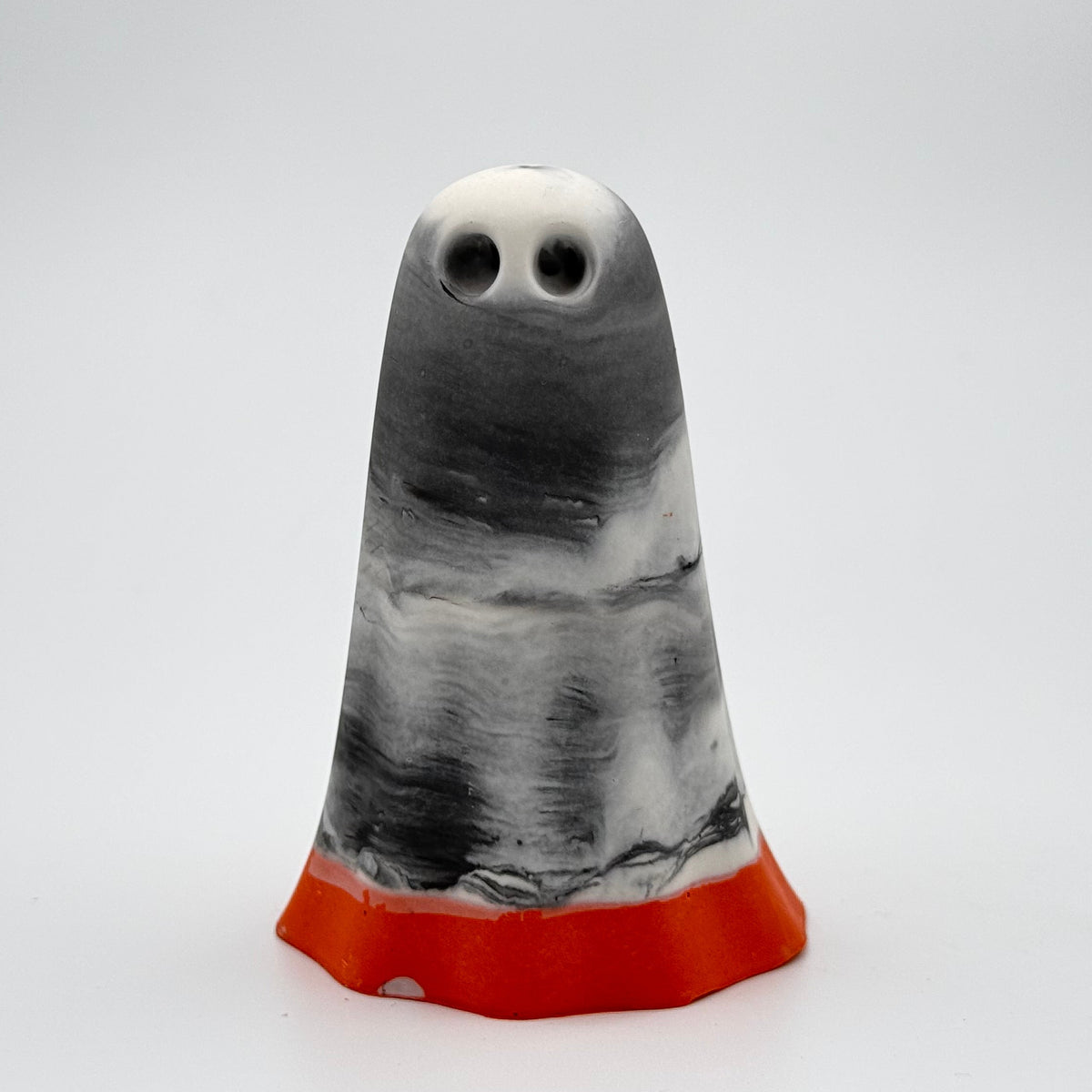 A handmade ghost figurine by The Nordic Ghost Merchants. The head and body of the ghost are a misty or smoky mix of grey and white. The bottom portion is a pumpkin orange shade. Front view on a grey studio background.