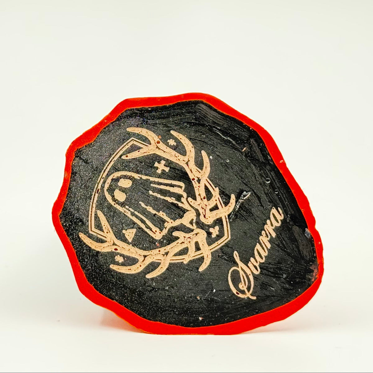 A handmade ghost figurine by The Nordic Ghost Merchants. The image is of the base of the ghost, engraved with the brand logo - a coat of arms with a sheet ghost in the centre.